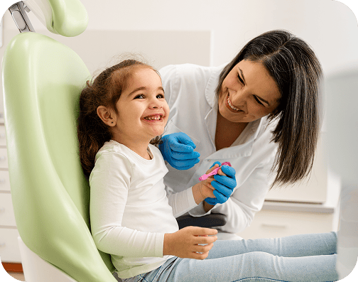 Girl sitting in a dentist chair as a pediatric dentist smiles at her