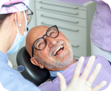 Older man sitting in dentist's chair as we converses with the hygienist 